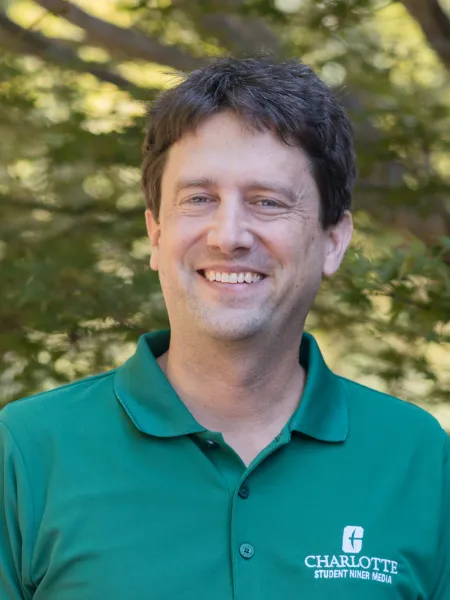 Profile photo of Justin Paprocki smiling, wearing a green polo shirt with the UNC Charlotte logo